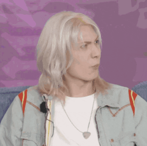 a man with long blonde hair is wearing a denim jacket and a necklace