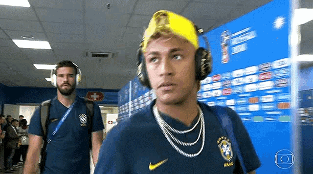 a man wearing headphones and a yellow hat is walking down a hallway