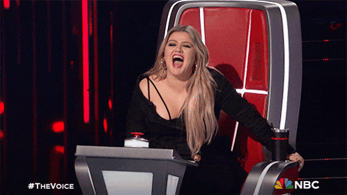 a woman is laughing while sitting in a chair with a nbc logo in the corner