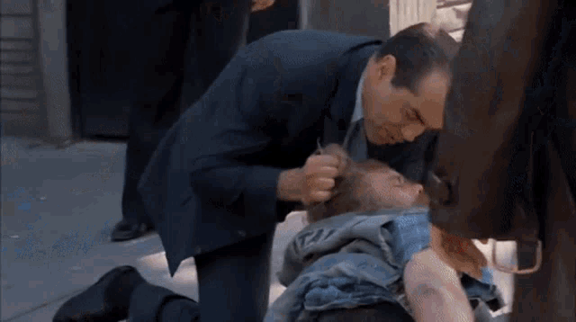 a man in a suit is kneeling down next to a man laying on the ground ..