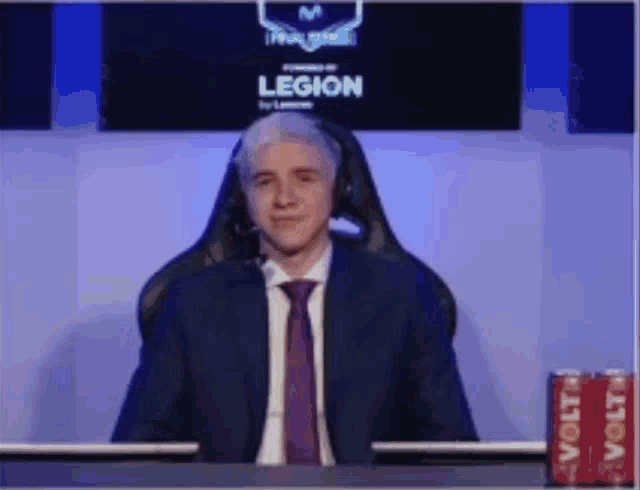 a man in a suit and tie is sitting at a desk in front of a sign that says legion