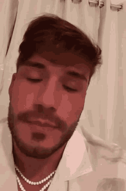 a man with a beard and a pearl necklace is wearing a white shirt and a pearl necklace .