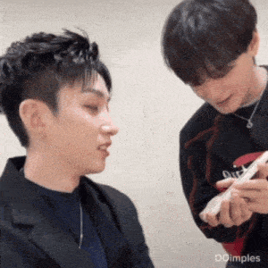 two young men are looking at a cell phone and one of them has dimples on his face
