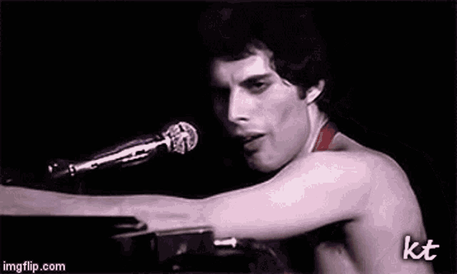 a man without a shirt is singing into a microphone while playing a piano .