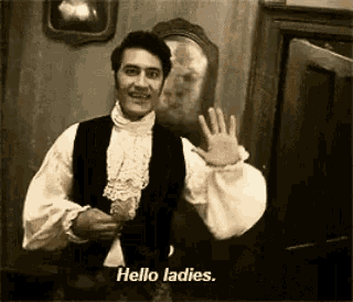 a man in a costume is waving his hand and saying `` hello ladies . ''