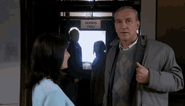 a man and a woman are standing in front of a door that says goods only