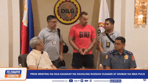 a man wearing a red shirt that says biwf stands in front of a group of men