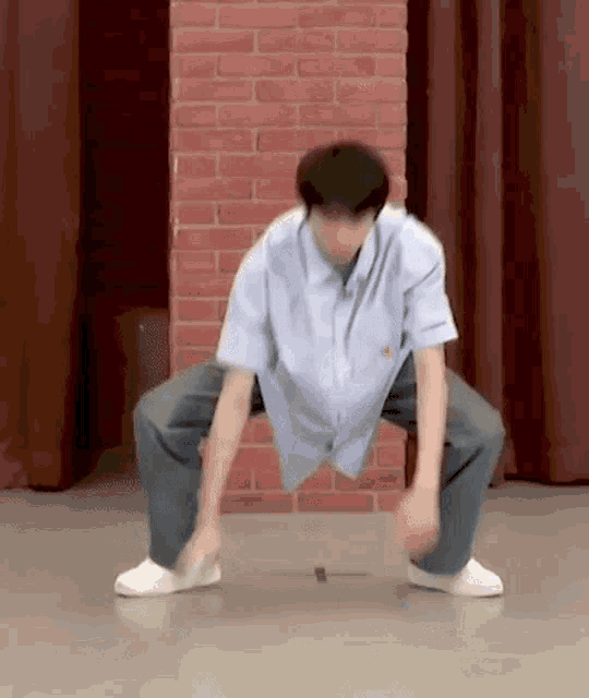 a man is squatting down in front of a red brick wall .