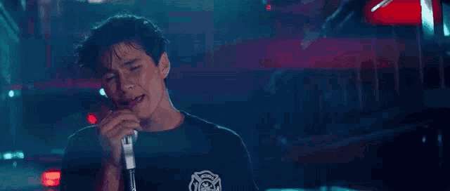 a young man is singing into a microphone in front of a fire truck in a dark room .