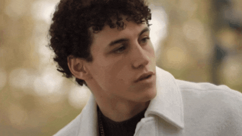 a young man with curly hair wearing a white jacket
