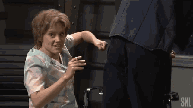 a woman in a wheelchair is standing next to a man in a snl shirt .