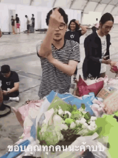 a man in a striped shirt is standing in front of a bunch of flowers and covering his face with his hand