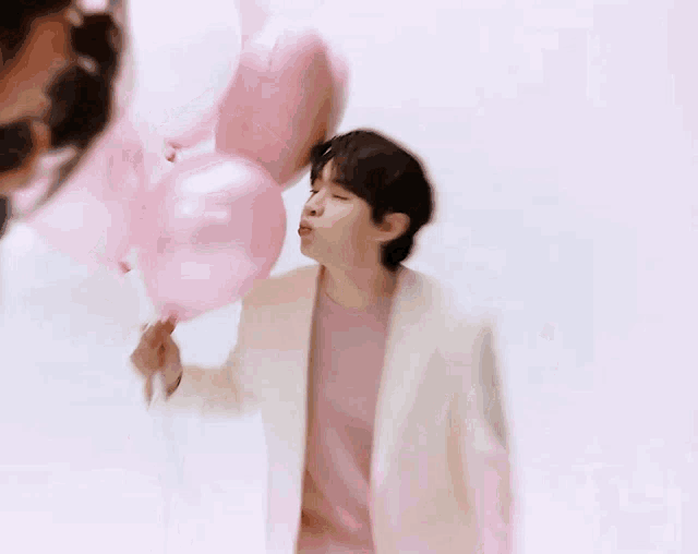 a man in a pink shirt is blowing a kiss while holding pink balloons