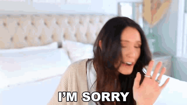 a woman is sitting on a bed making a funny face and saying `` i 'm sorry '' .