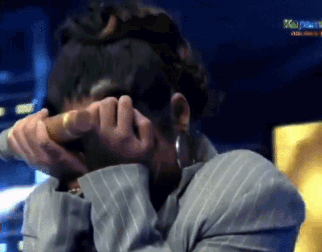 a person covering their face with their hands with a sign in the background that says ' saigon tv '
