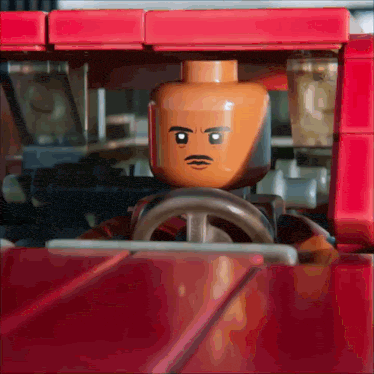 a lego man with a mustache is driving a red vehicle