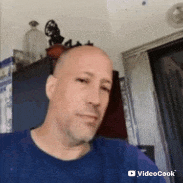 a bald man with a beard is wearing a blue shirt and making a funny face .