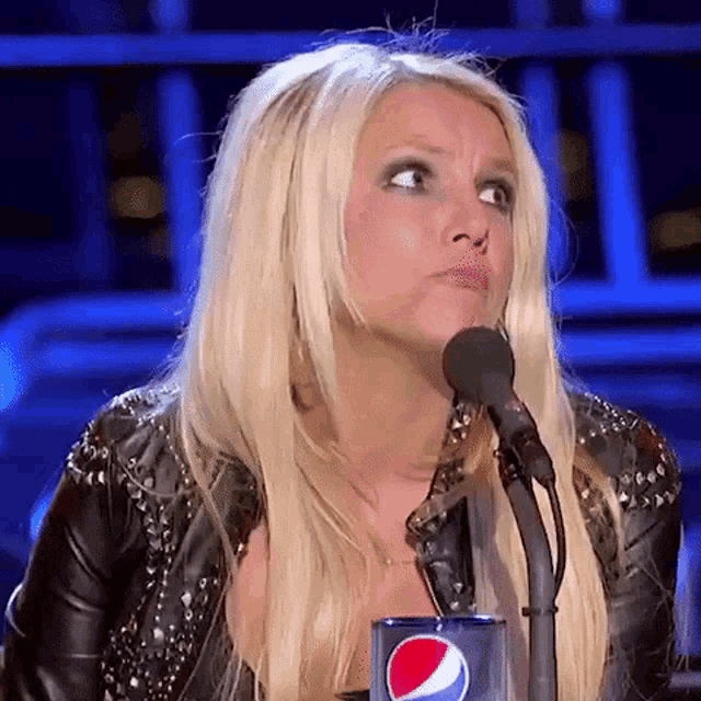 a blonde woman is standing in front of a microphone with a pepsi can in front of her