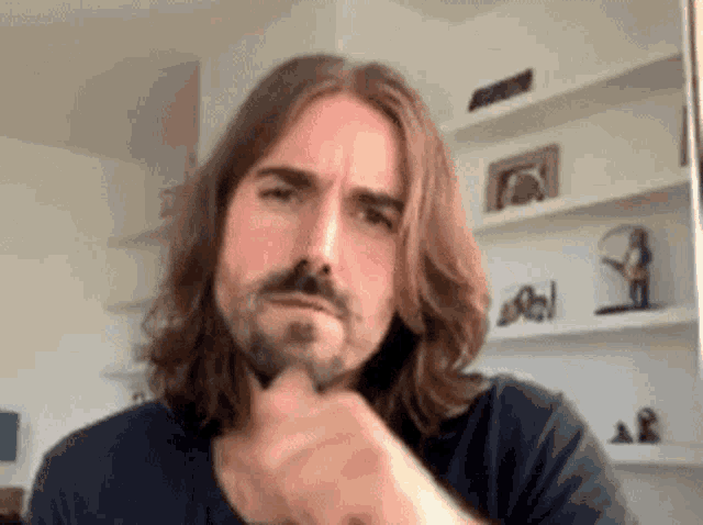 a man with long hair and a beard is making a face with his hand