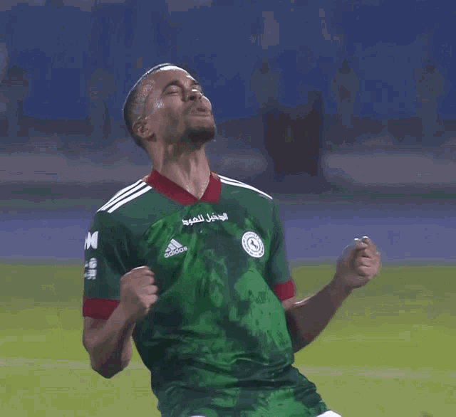 a man wearing a green adidas shirt stands on a field