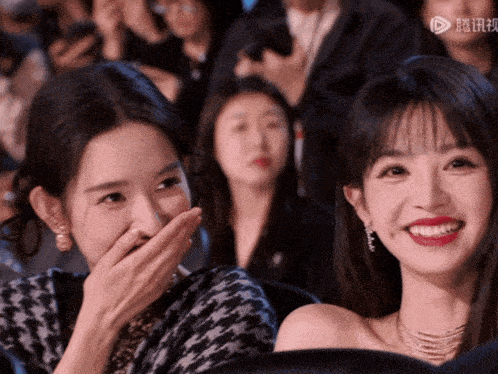 a woman covering her mouth with her hand while another woman looks on