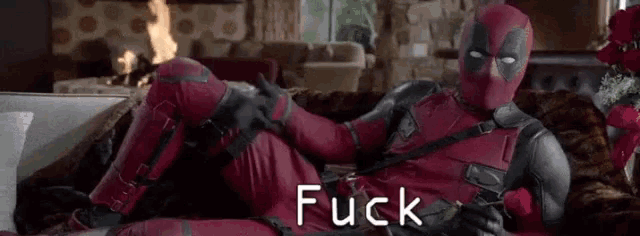deadpool is laying on a couch in a living room holding a rose and giving a thumbs up .