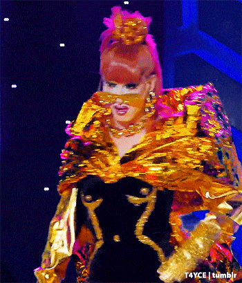 a drag queen with red hair is wearing a gold and black costume .