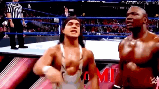 two wrestlers are standing in a wrestling ring with a referee behind them .