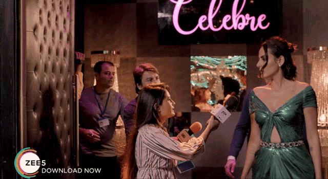 a woman in a green dress is being interviewed by a woman with a microphone in front of a sign that says celebrate