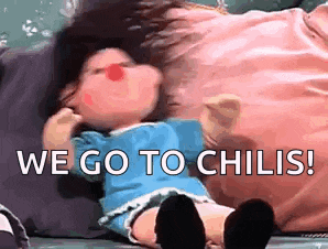 a doll with a red nose is laying on a pillow with the words `` we go to chilis '' written on it .