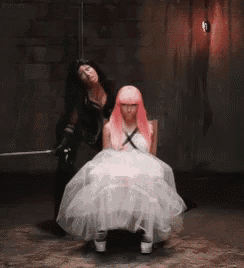 a woman in a white dress is sitting in a chair next to a woman with pink hair .