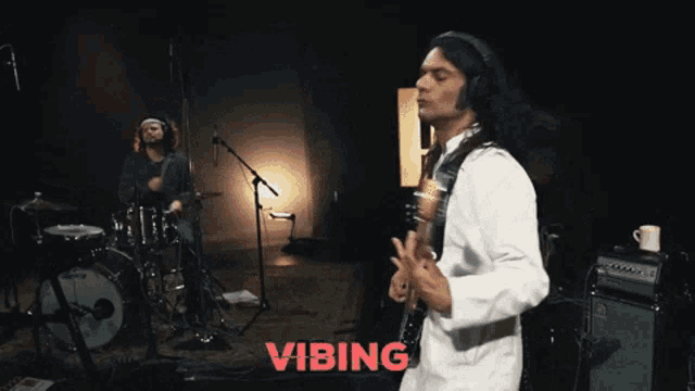 a man is playing a guitar in front of a drum set and the word vibing is on the bottom right