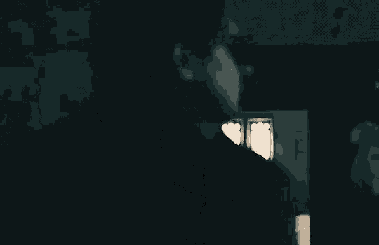 a man in a black shirt is standing in the dark in front of a window .