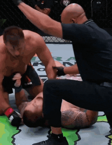 a referee is kneeling down next to a fighter whose shorts say reebok on them