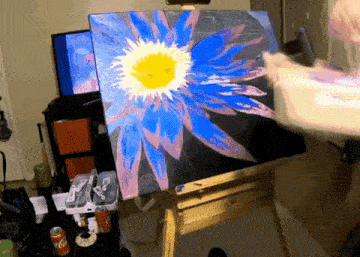a painting of a blue flower with a yellow center is on an easel