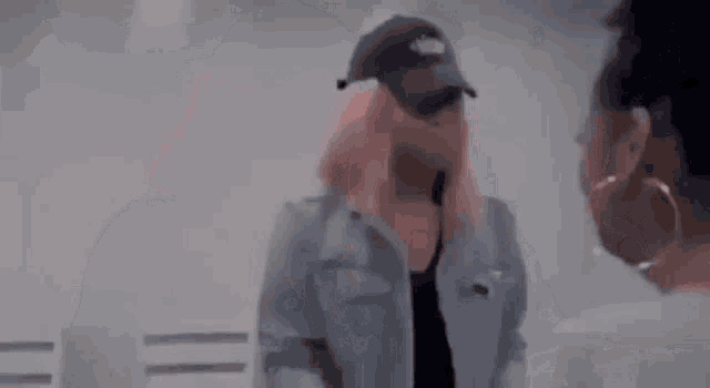 a woman with pink hair and a hat is standing next to another woman .