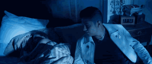 a man in a white jacket sits next to a woman in a bed with a clock that says 11:12 on it