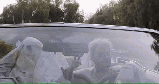 a man giving a peace sign while driving a convertible car