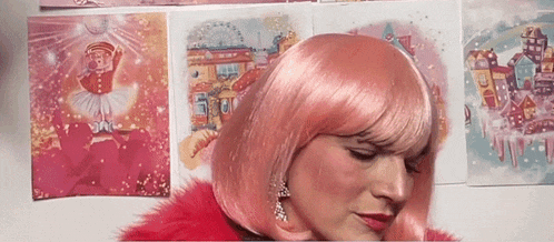 a woman wearing a pink wig and earrings is sitting in front of a wall with paintings on it .