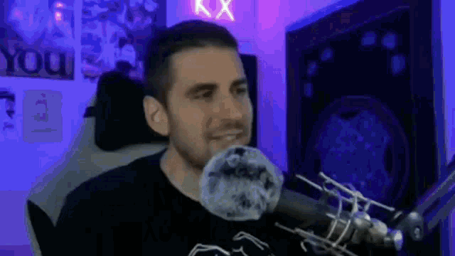 a man is sitting in front of a microphone in a room with purple lights .