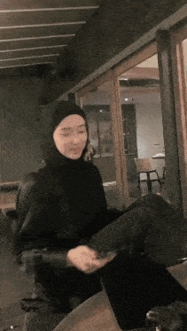 a woman wearing a hijab and a black jacket is sitting in front of a glass door .
