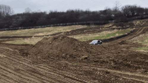 a white car is driving through a dirt field with a fence in the background