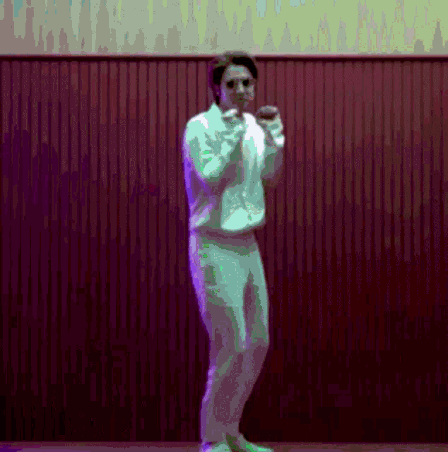 a man in a white sweatshirt and white pants stands in front of a red wall
