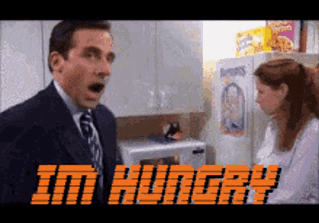 a man in a suit and tie says i 'm hungry while standing next to a woman in a kitchen