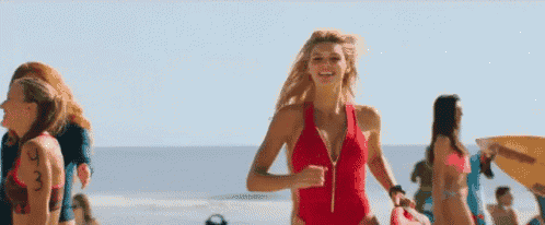 a woman in a red swimsuit is running on a beach with a surfboard .