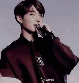 a young man is singing into a microphone while wearing a maroon jacket .
