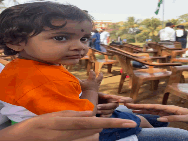 a little girl in an orange shirt is being held by someone