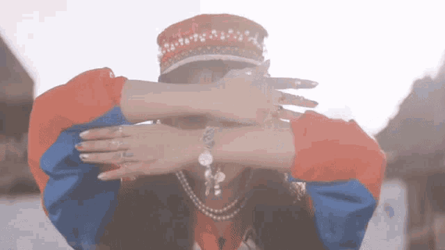 a woman is covering her face with her hands while wearing a hat and a bracelet .