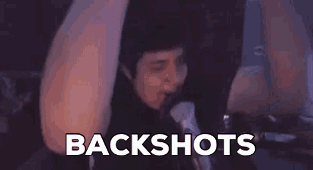 a person is sitting in a chair with their arms in the air and the words backshots written on the screen behind them .