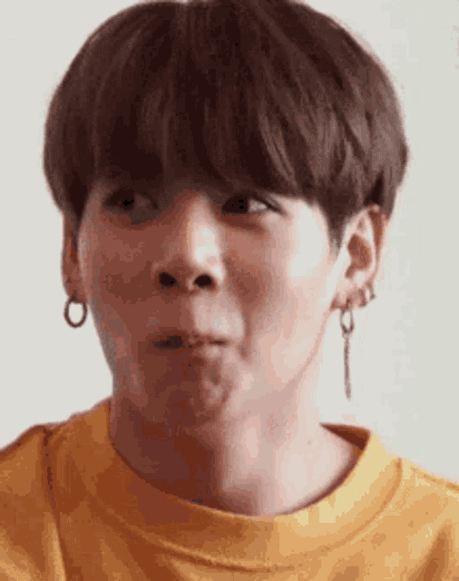 a young man wearing a yellow shirt and earrings is making a face .